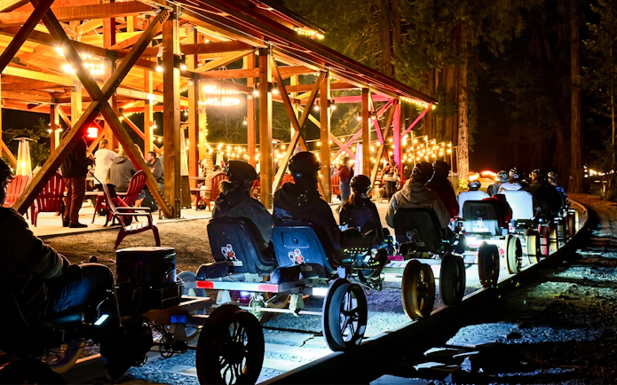 Visitors on rail bikes near Glen Blair Bar, San Francisco, illuminated by string lights at night.
