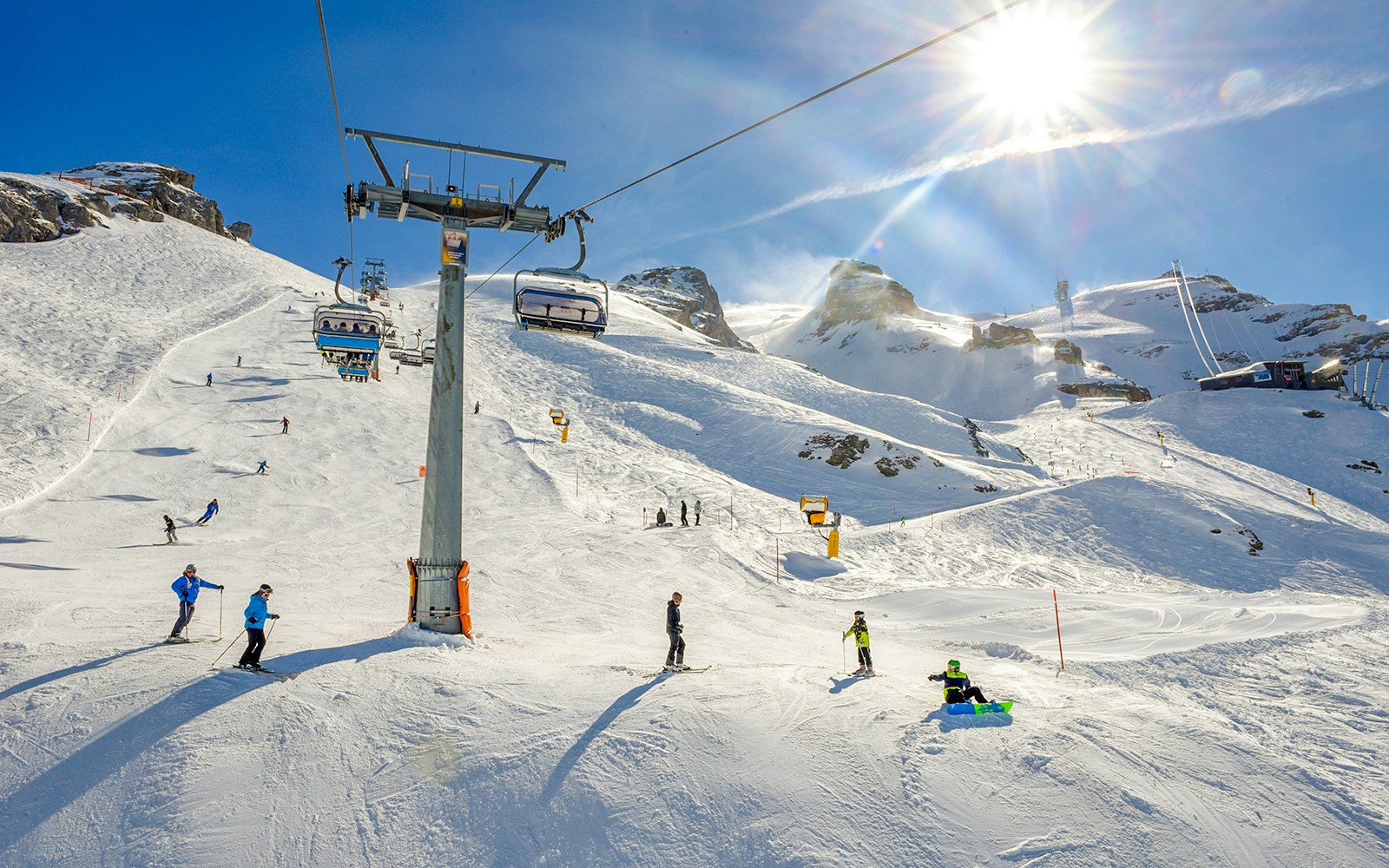 Skiers and snowboarders on Mount Titlis slopes with chairlift under sunny sky.