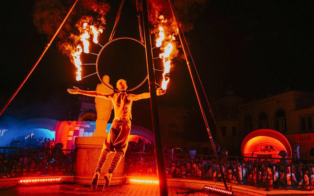 Fire performer at Sparty bath party in Budapest with colorful lights and crowd.