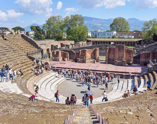 Tourists exploring ancient ruins in Pompeii under a clear blue sky on a full-day tour from Naples.