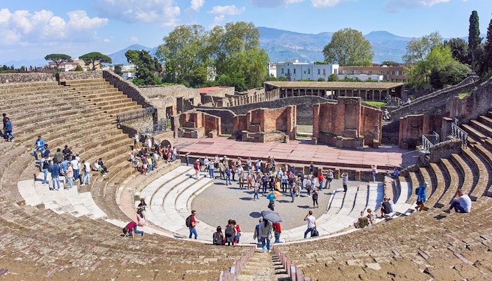 Tourists exploring ancient ruins in Pompeii under a clear blue sky on a full-day tour from Naples.