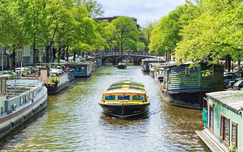 Canal boat cruising through Amsterdam with houseboats and bridge in view.