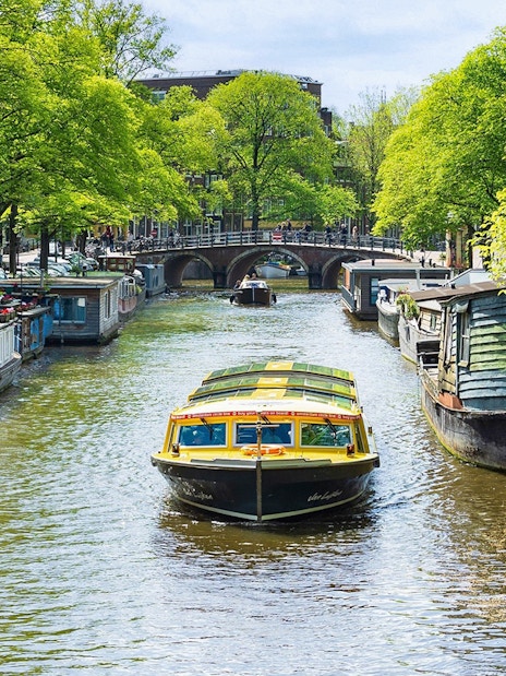 Canal boat cruising through Amsterdam with houseboats and bridge in view.