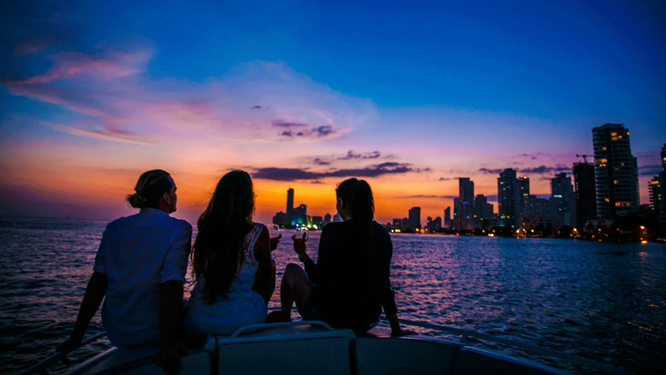 Boat party at sunset in Cartagena Bay with city skyline in view.