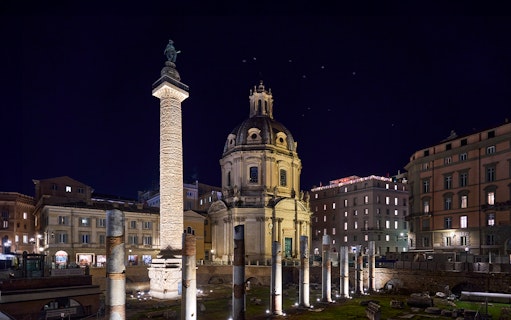 Roman Forum at night with illuminated columns and historic architecture.