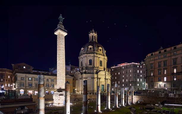 Roman Forum at night with illuminated columns and historic architecture.