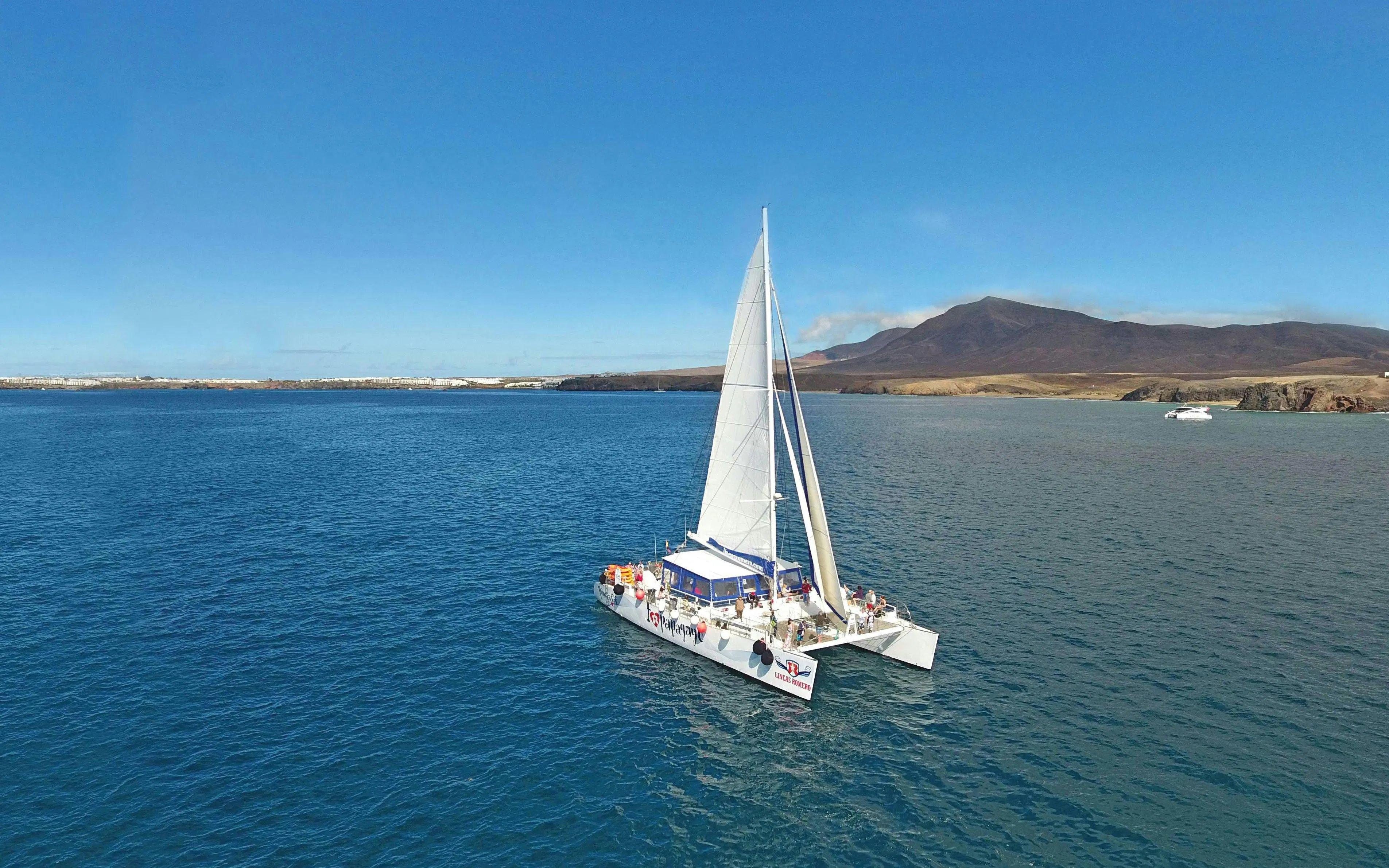 Catamaran sailing near Papagayo Beaches, Lanzarote, with distant mountains in view.