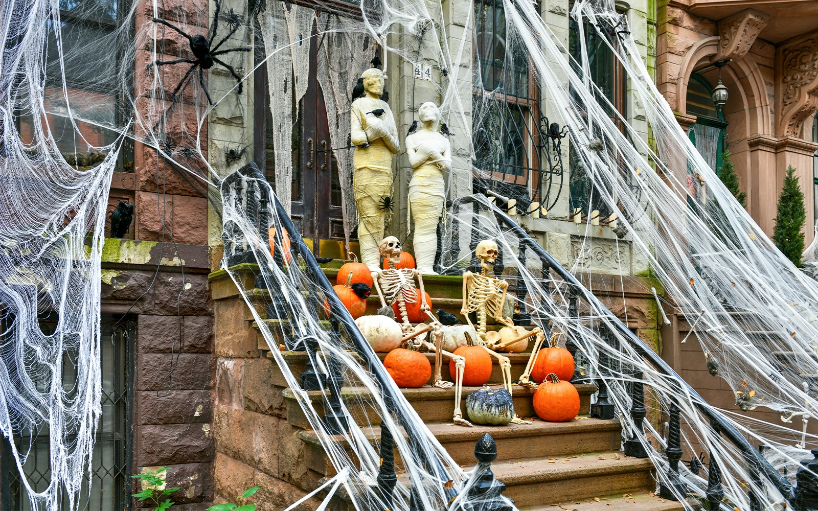Halloween decorations with skeletons, pumpkins, and cobwebs on a New York City brownstone stoop.