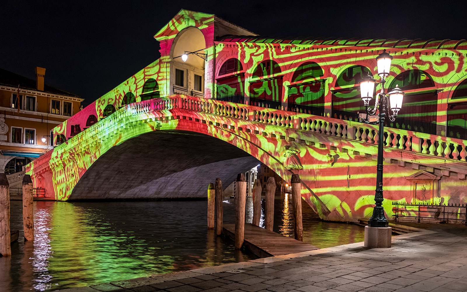 Rialto Bridge in Venice illuminated with colorful Christmas lights at night.