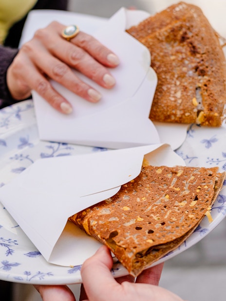 Hands holding a plate with folded crepes during Emily in Paris Food Tour.