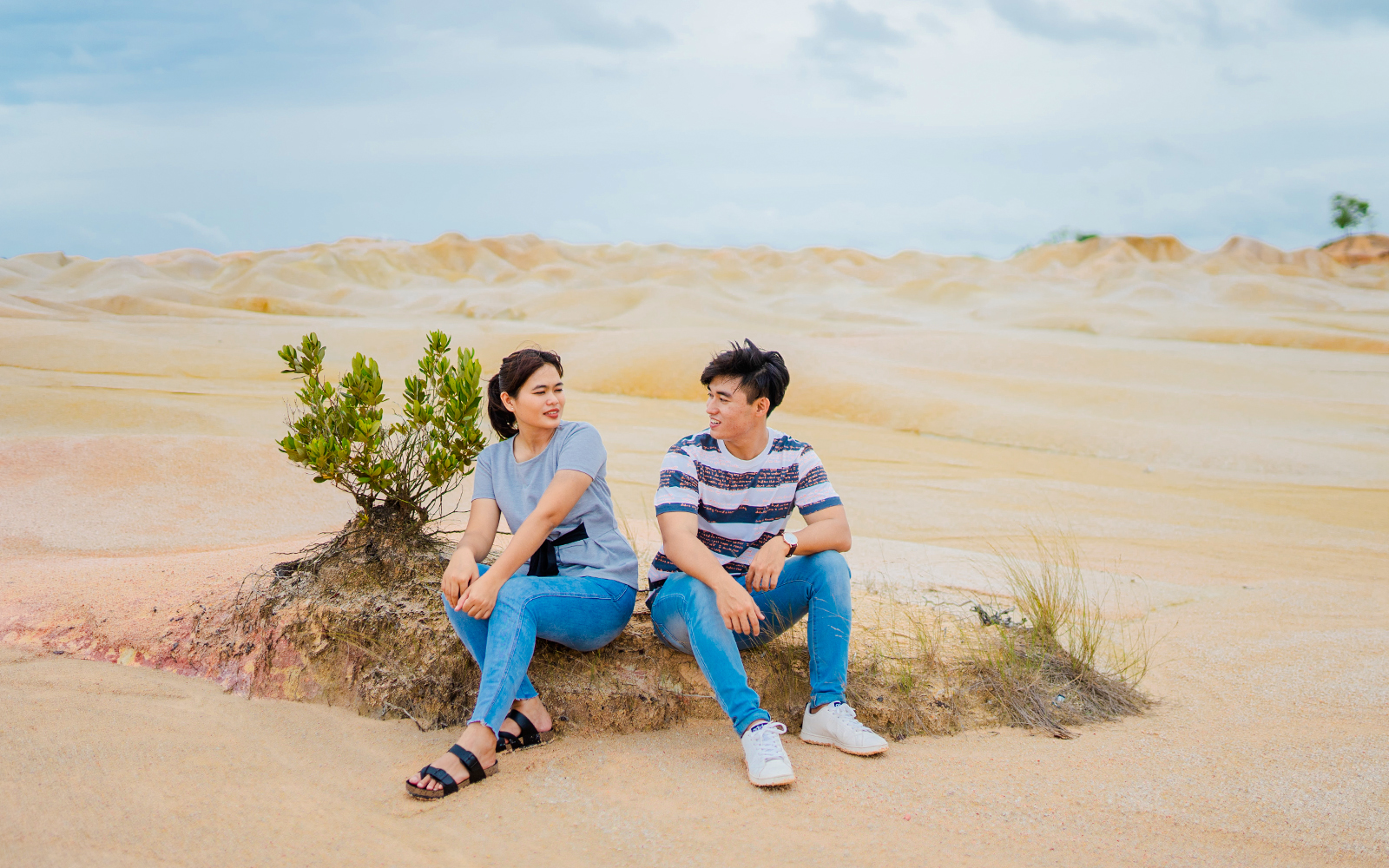 Couple sitting on a rock at Bintan Mini Desert with sandy landscape.