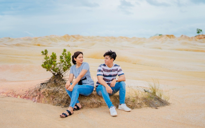Couple sitting on a rock at Bintan Mini Desert with sandy landscape.