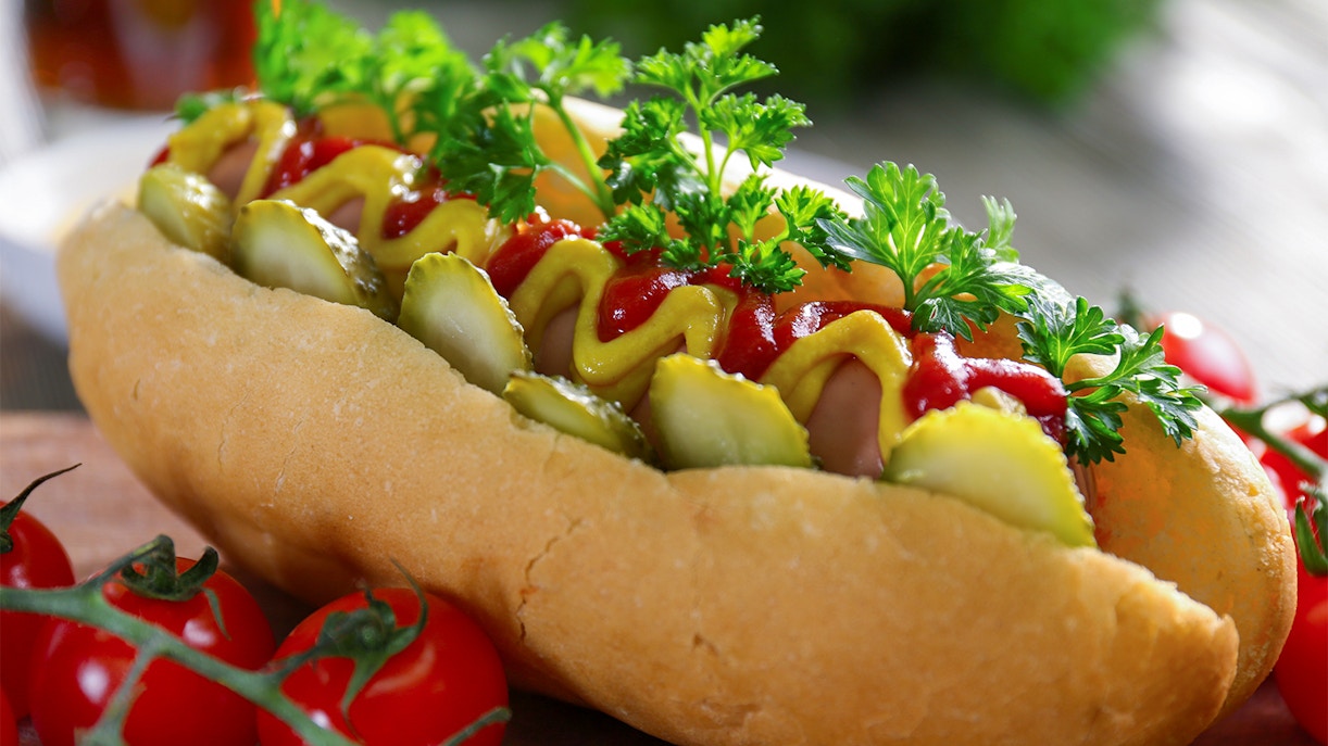 Hot dog with mustard, ketchup, pickles, and parsley