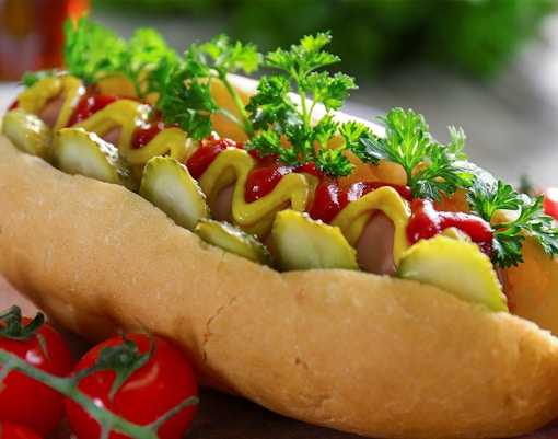 Hot dog with mustard, ketchup, pickles, and parsley