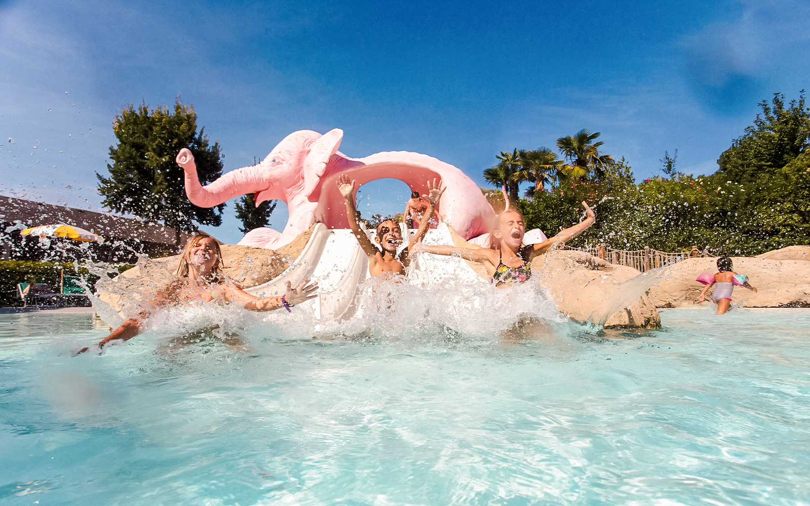 Children enjoying a water slide at Aquafan Water Park with a pink elephant sculpture.