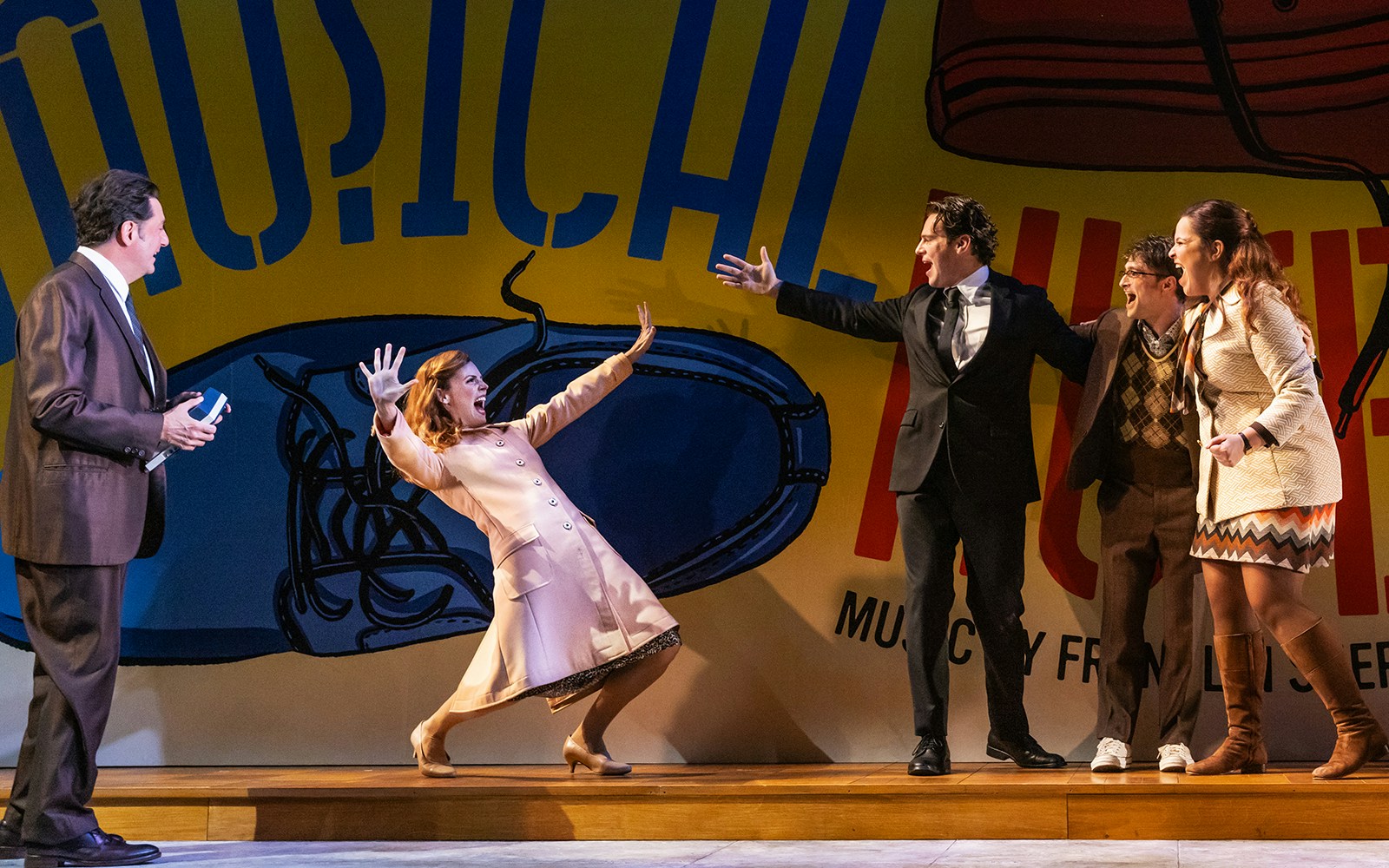 Performers on stage in a scene from "Merrily We Roll Along" musical.