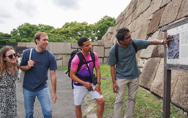 Tourists examining a map at the Imperial Palace, Tokyo, with stone walls in the background.