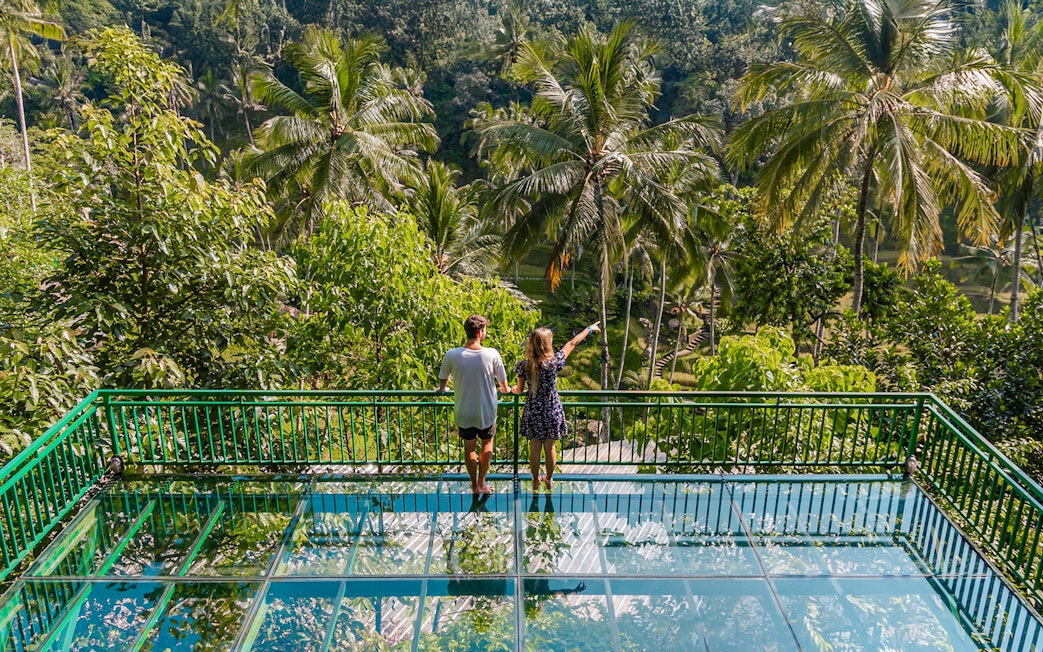 Couple on glass terrace overlooking lush greenery at Alas Harum Bali.