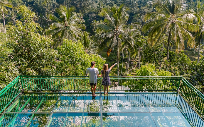 Couple on glass terrace overlooking lush greenery at Alas Harum Bali.
