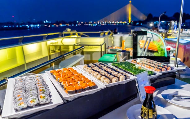 Sushi buffet on Alangka Dinner Cruise at IconSiam Pier No.4 with city lights in background.