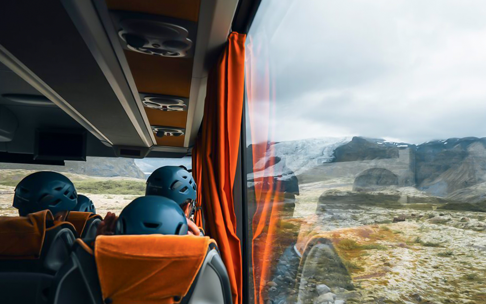 Bus interior with passengers wearing helmets, viewing glacier landscape through window.