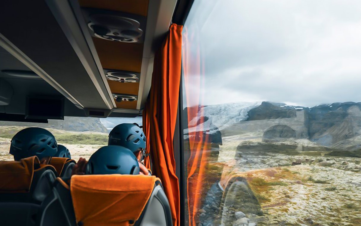 Bus interior with passengers wearing helmets, viewing glacier landscape through window.