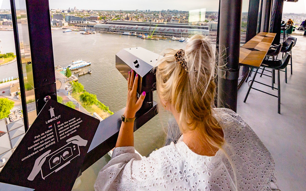 Person using a viewer at ADAM Lookout indoor panorama deck, overlooking Amsterdam.
