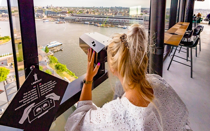 Person using a viewer at ADAM Lookout indoor panorama deck, overlooking Amsterdam.