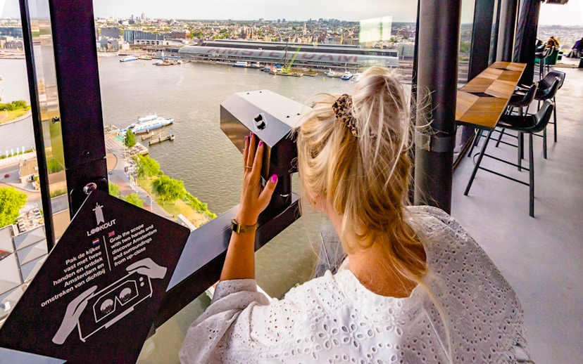 Person using a viewer at ADAM Lookout indoor panorama deck, overlooking Amsterdam.