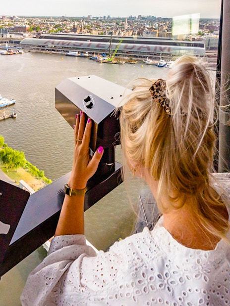Person using a viewer at ADAM Lookout indoor panorama deck, overlooking Amsterdam.