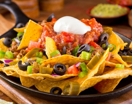 Nachos with cheese, salsa, olives, jalapeños, and sour cream on a skillet.