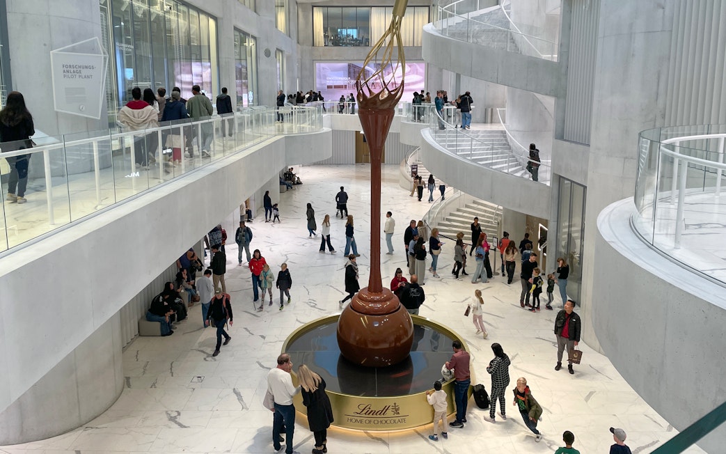 Visitors inside Lindt Home of Chocolate Museum Zurich, viewing large chocolate fountain.