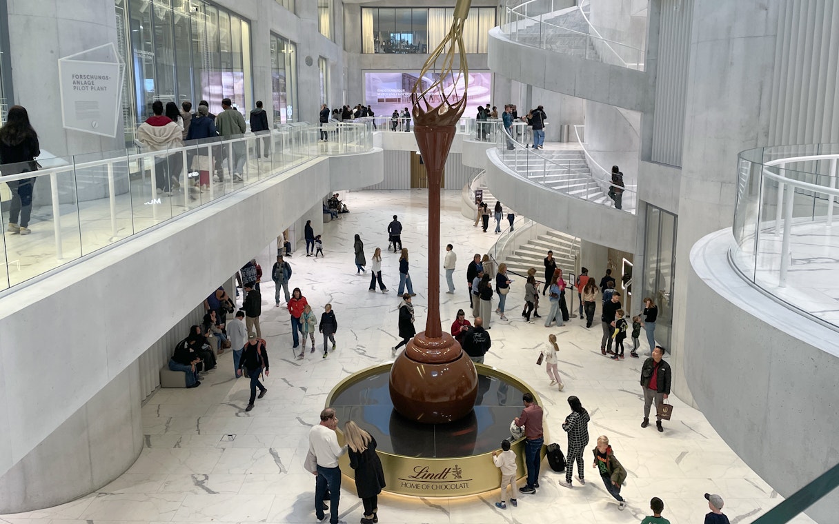Visitors inside Lindt Home of Chocolate Museum Zurich, viewing large chocolate fountain.