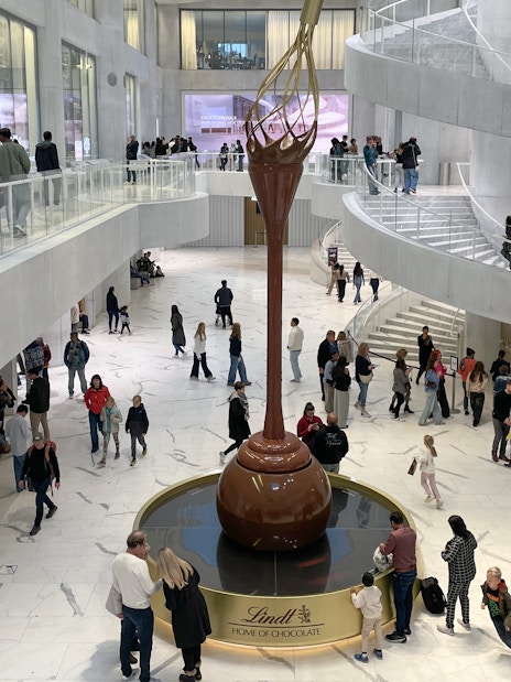 Visitors inside Lindt Home of Chocolate Museum Zurich, viewing large chocolate fountain.