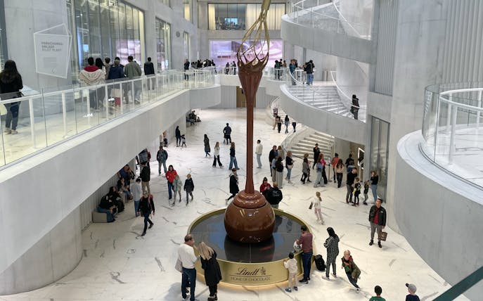 Visitors inside Lindt Home of Chocolate Museum Zurich, viewing large chocolate fountain.