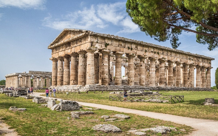 Tourists exploring ancient Greek temple ruins in Archaeological Park of Paestum, Italy.