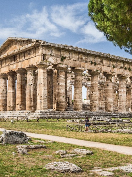 Tourists exploring ancient Greek temple ruins in Archaeological Park of Paestum, Italy.