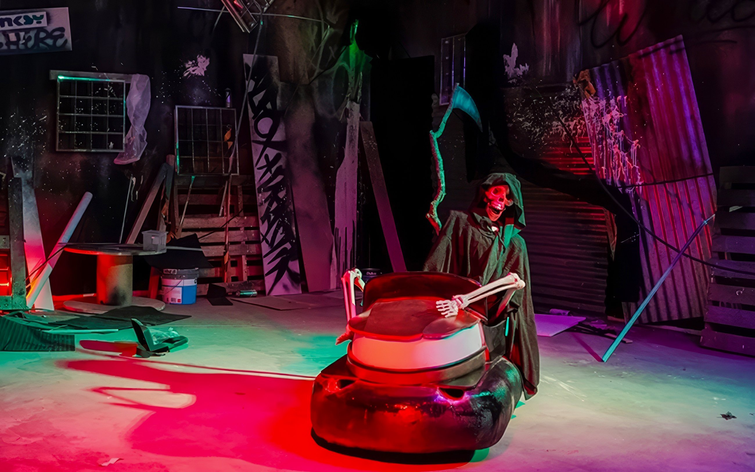 Skeleton in a cloak driving a bumper car in a dimly lit, graffiti-covered room at Banksy Limitless.