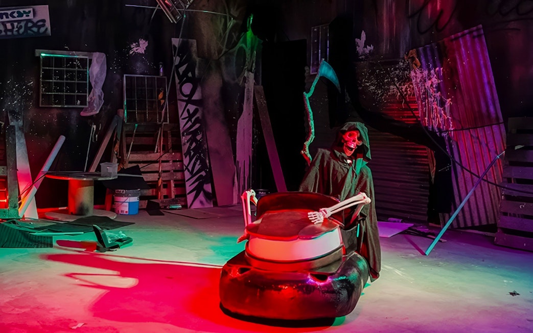 Skeleton in a cloak driving a bumper car in a dimly lit, graffiti-covered room at Banksy Limitless.