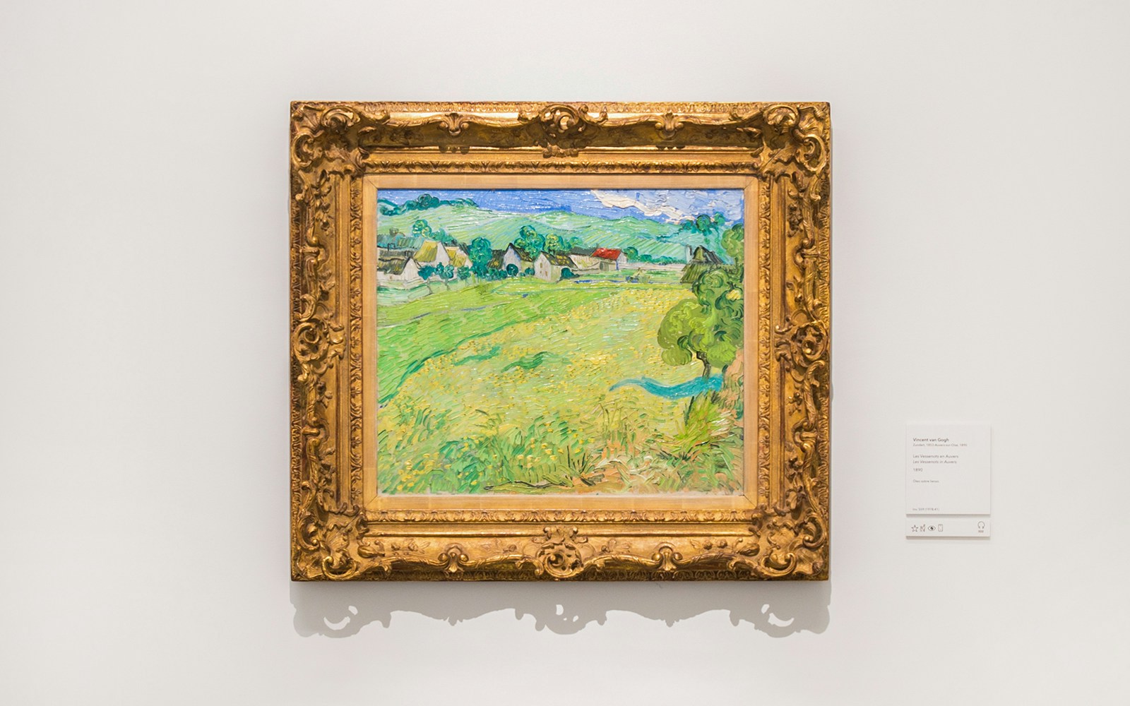 Painting of a countryside landscape by Vincent van Gogh in a gold frame at a museum.