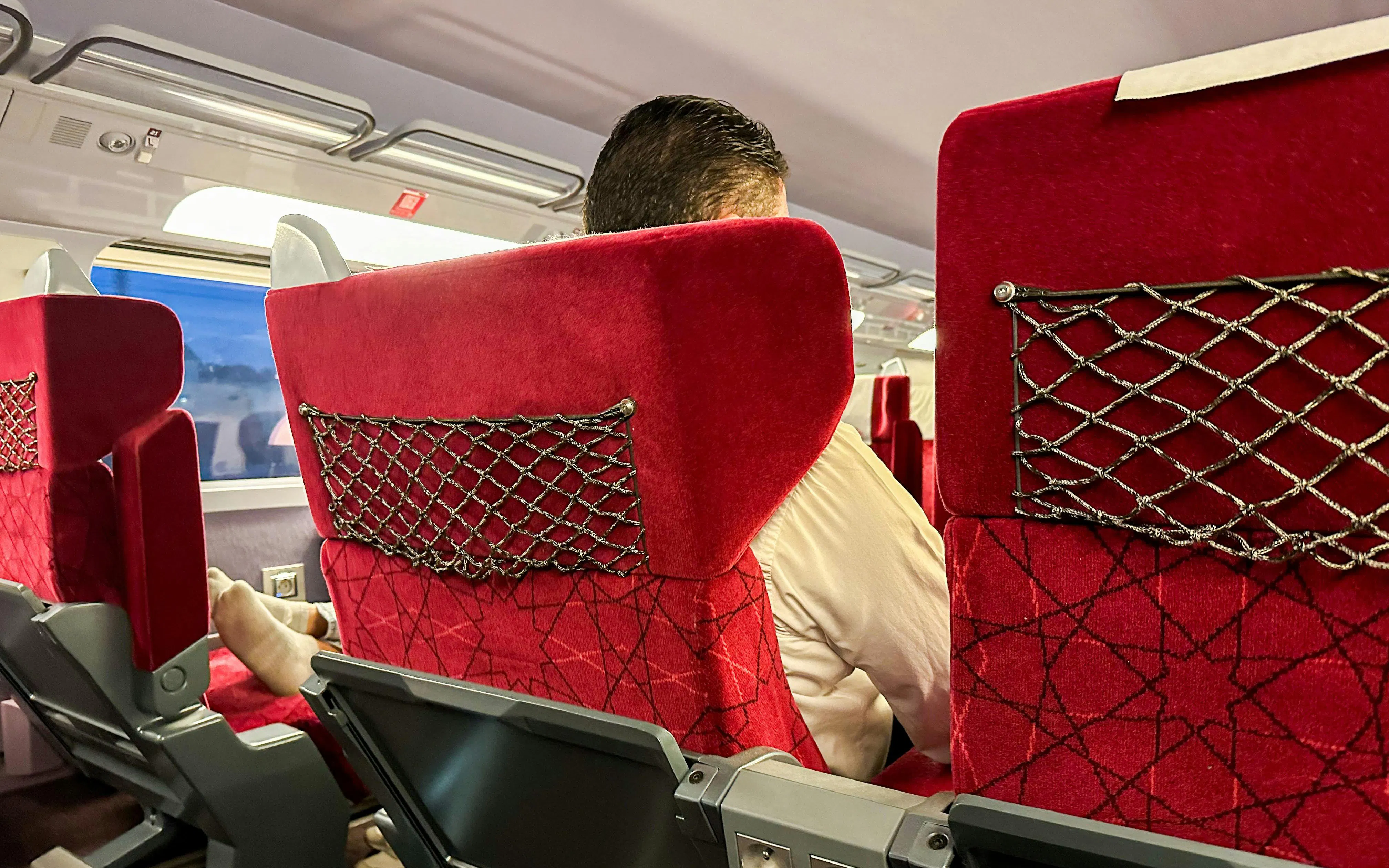 Interior view of Al Boraq high-speed train with red seats and passenger.