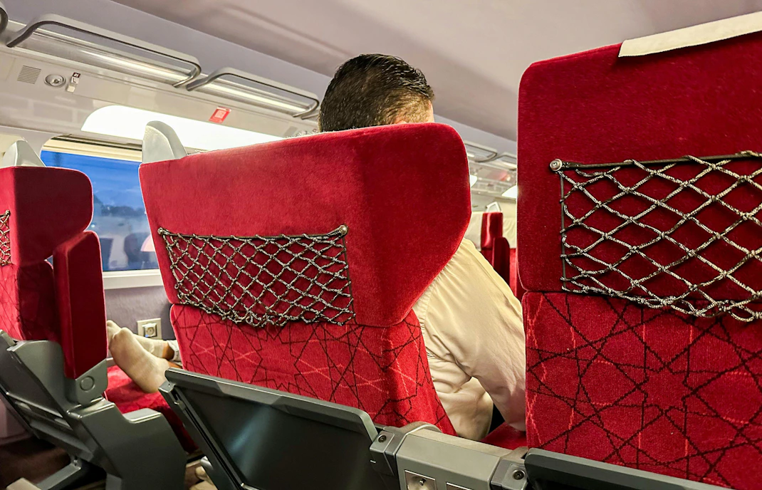 Interior view of Al Boraq high-speed train with red seats and passenger.
