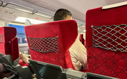 Interior view of Al Boraq high-speed train with red seats and passenger.
