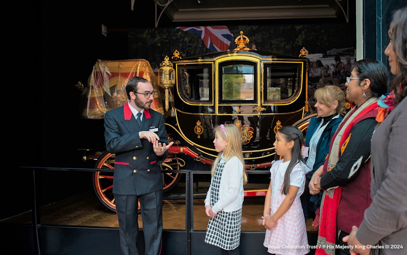 Warden explaining to family visitors in front of a royal carriage at The Royal Mews.