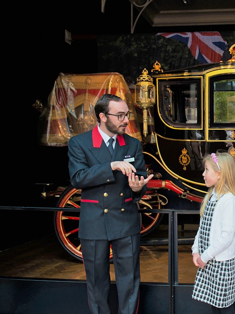 Warden explaining to family visitors in front of a royal carriage at The Royal Mews.