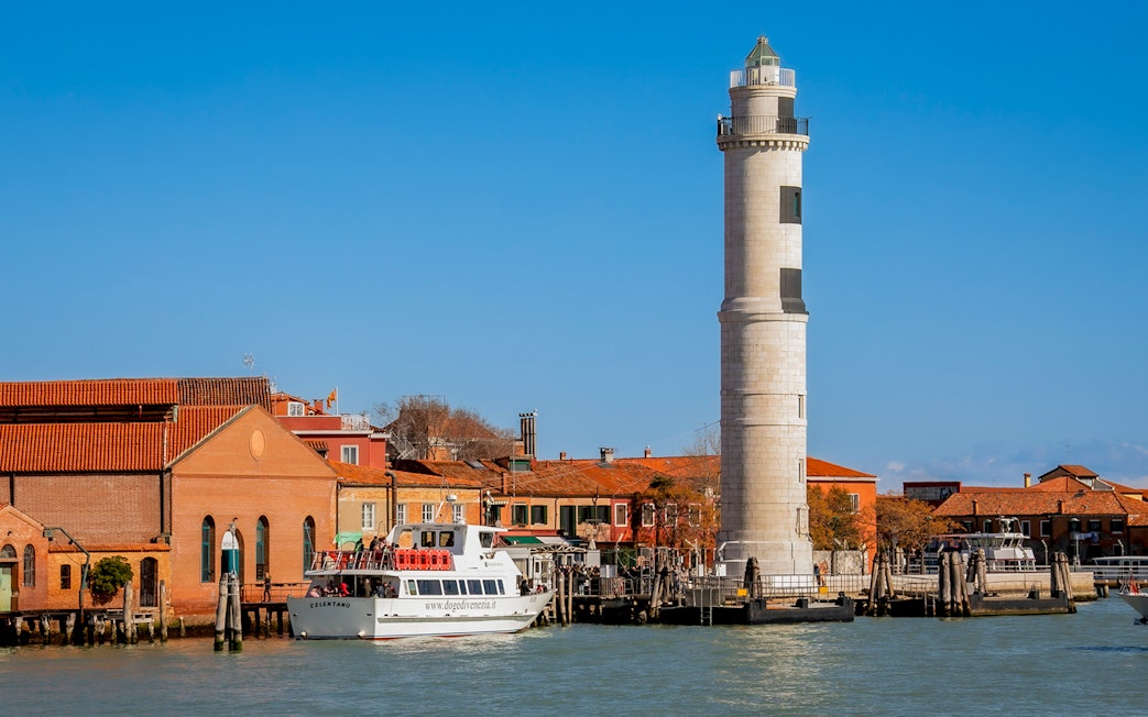 Tour boat near Murano lighthouse and colorful buildings, Murano Island, Italy.