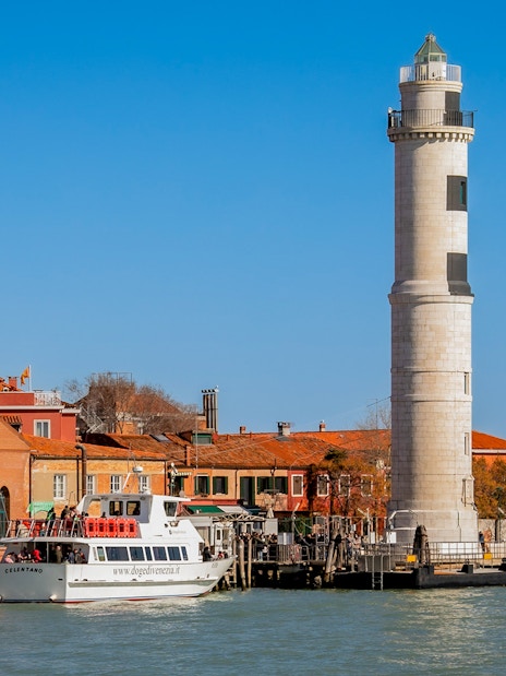 Tour boat near Murano lighthouse and colorful buildings, Murano Island, Italy.