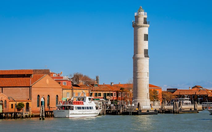 Tour boat near Murano lighthouse and colorful buildings, Murano Island, Italy.