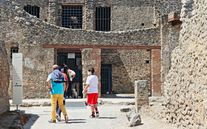 Visitors entering ancient stone building on Pompeii guided tour, Italy.