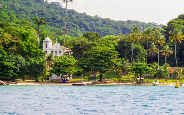 Colonial church and palm trees by the shore at Freguesia Beach, Ilha Grande, Brazil.